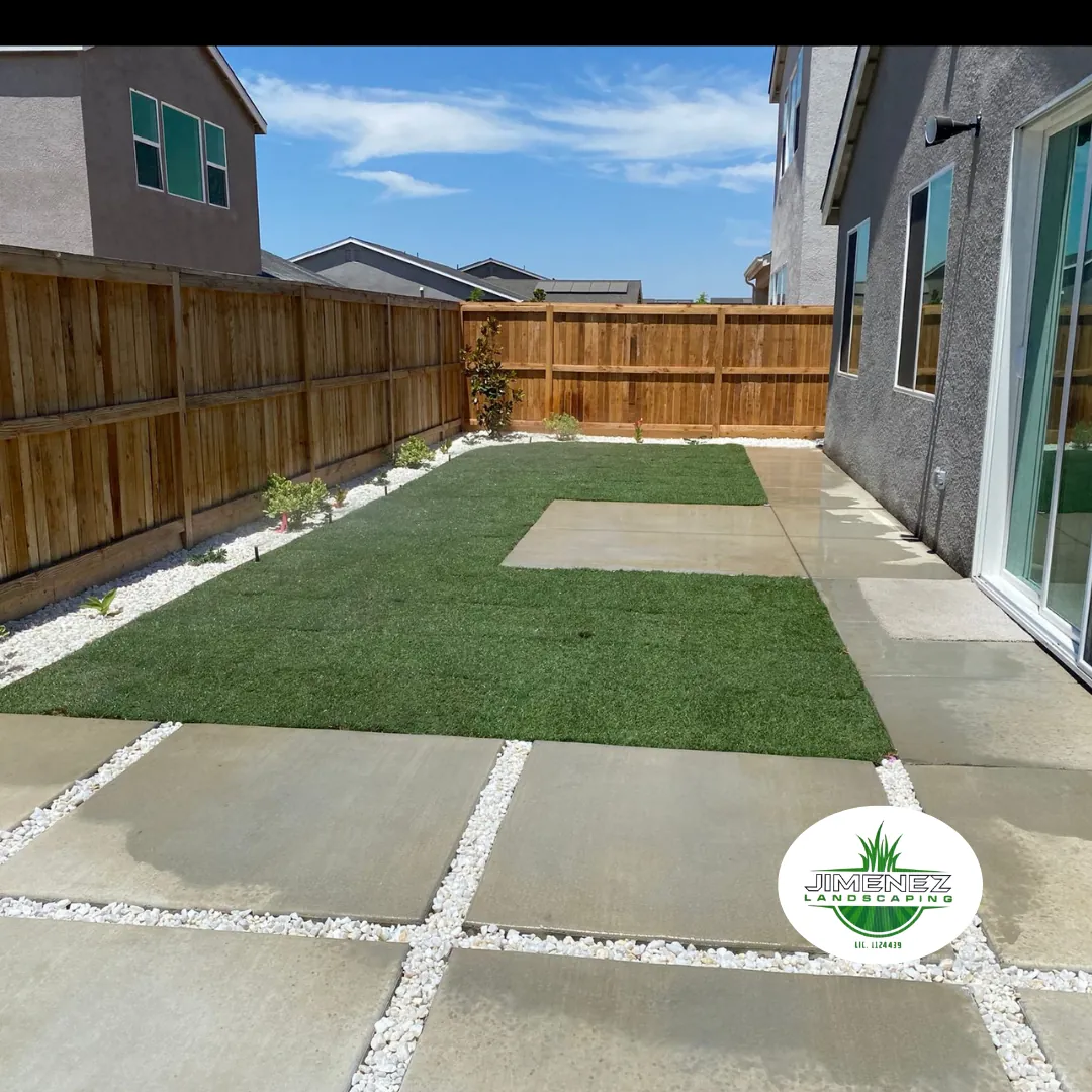 Backyard landscape featuring artificial turf and decorative rock borders, with a wooden fence and concrete patio, showcasing Jimenez Landscaping's expertise in enhancing outdoor spaces in Bakersfield.