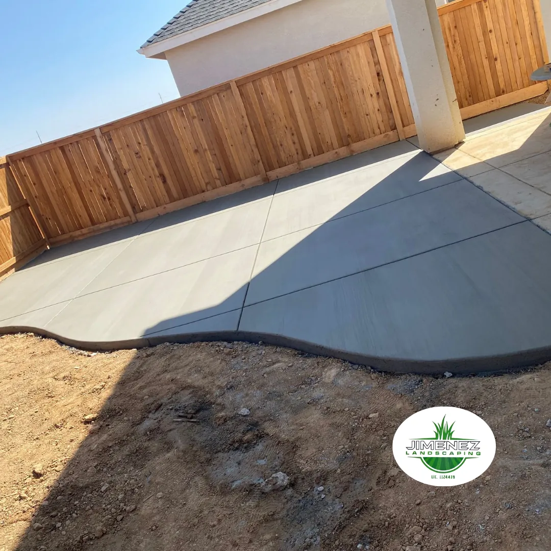 Freshly poured concrete patio with curved edges, surrounded by wooden fencing, showcasing Jimenez Landscaping's concrete services in Bakersfield.