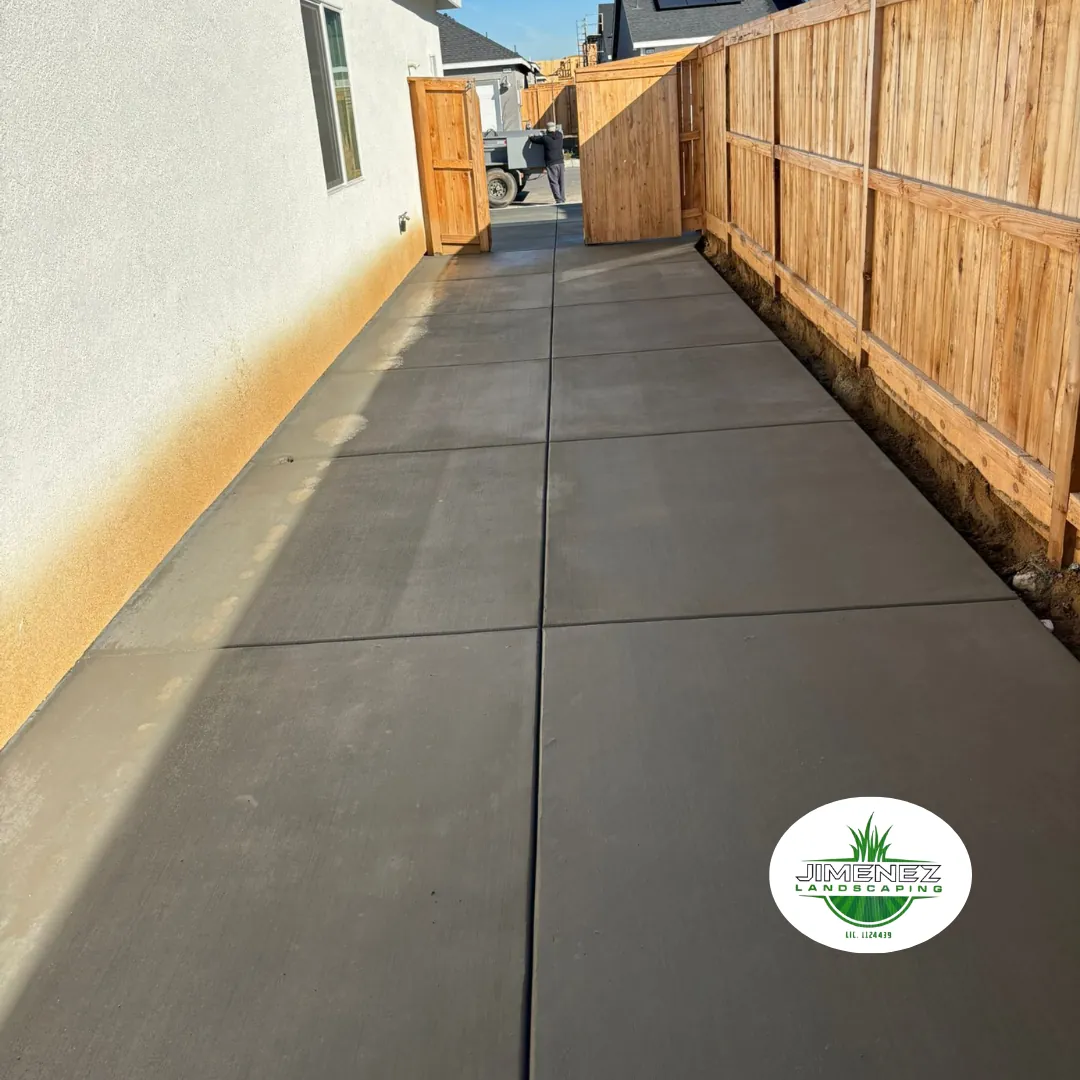 Concrete walkway installation by Jimenez Landscaping, showcasing a smooth, durable surface alongside a residential property in Bakersfield, framed by wooden fencing and a side entrance.
