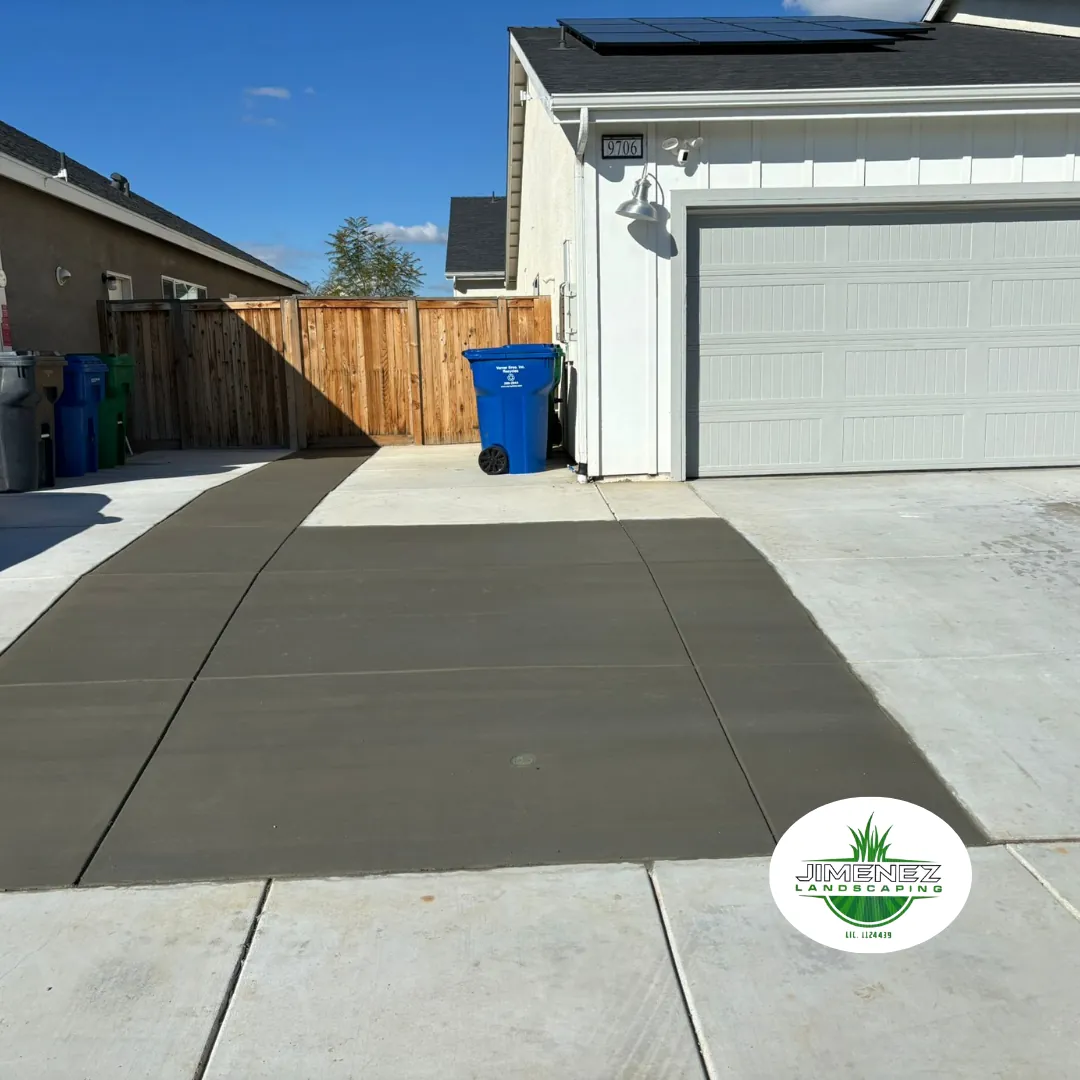 Concrete driveway installation by Jimenez Landscaping in Bakersfield, showcasing a smooth, freshly poured surface adjacent to a garage and wooden fence.