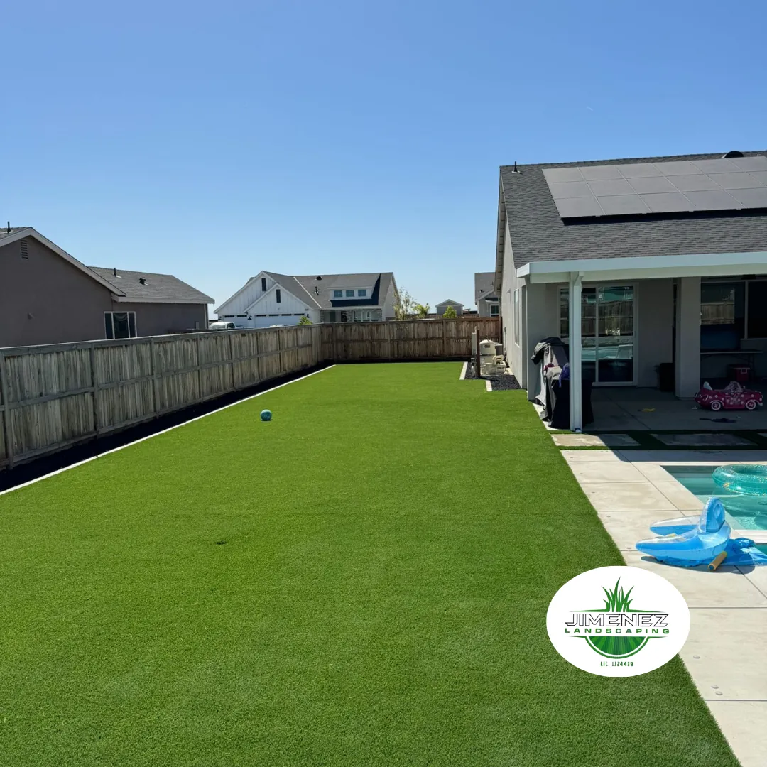 Artificial turf installation in a backyard, showcasing a vibrant green lawn surrounded by a wooden fence and residential homes, highlighting Jimenez Landscaping's expertise in Bakersfield.