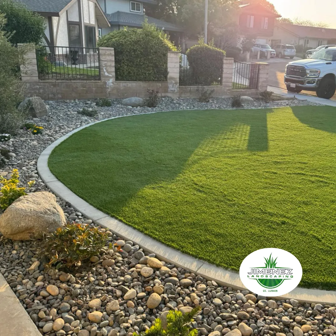 Artificial turf lawn installation with decorative rock and landscaping design by Jimenez Landscaping in Bakersfield, showcasing a vibrant green lawn bordered by a stone pathway and lush plantings.