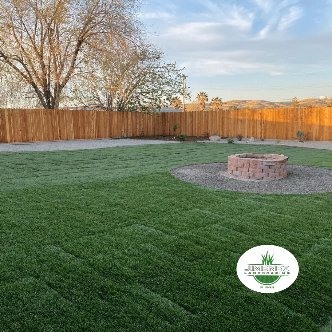 Lush green artificial turf surrounding a stone fire pit in a spacious backyard, showcasing Jimenez Landscaping's expertise in landscape design for Bakersfield.
