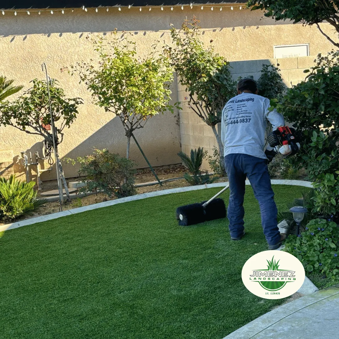 Worker applying artificial turf in a landscaped backyard, showcasing professional landscape installation services by Jimenez Landscaping in Bakersfield, California.