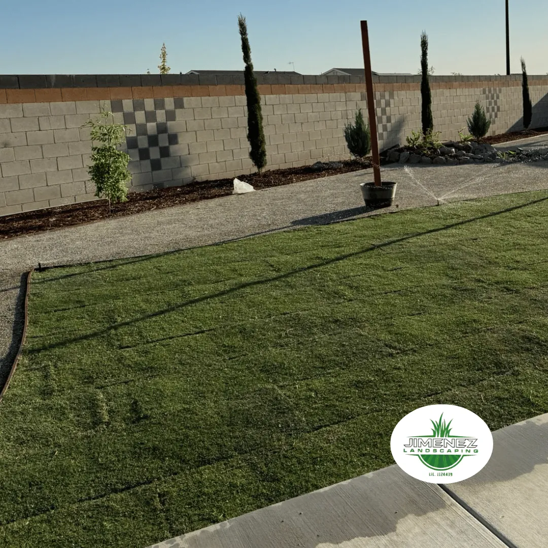 Artificial turf installation in a landscaped yard with a gravel pathway, featuring trees along a cinder block wall, showcasing Jimenez Landscaping branding.