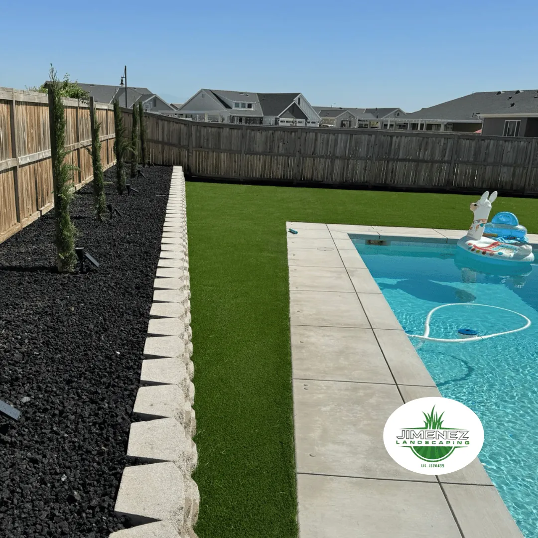 Modern backyard featuring energy-efficient artificial turf, decorative black rock, and a swimming pool, designed by Jimenez Landscaping in Bakersfield.