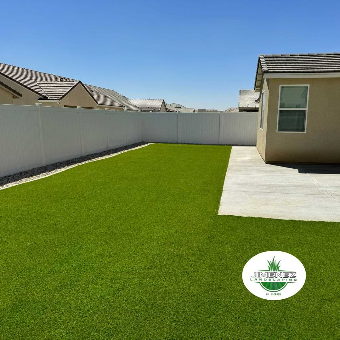Lush artificial turf installation in a residential backyard, showcasing a vibrant green lawn surrounded by a white fence and concrete patio, highlighting low-maintenance landscaping solutions in Bakersfield.