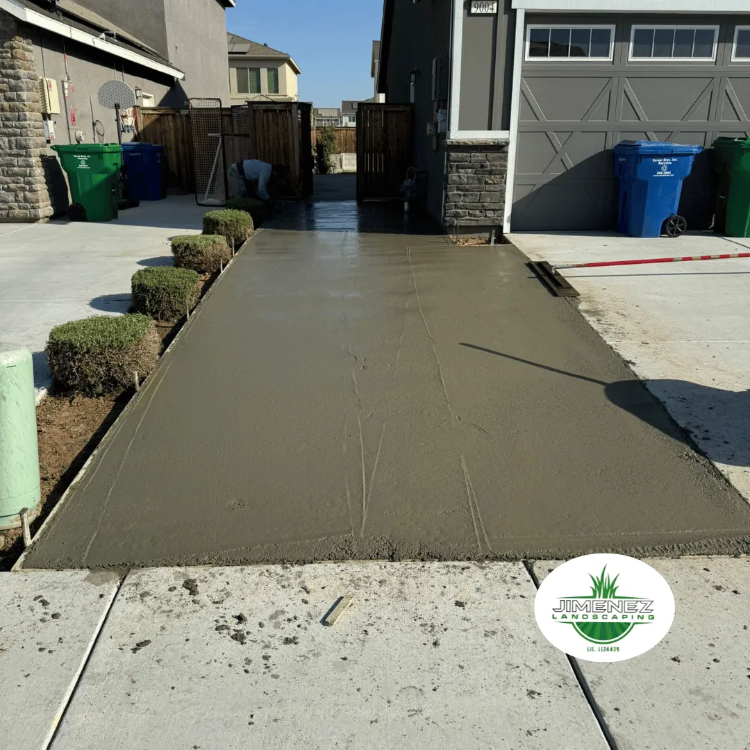 Concrete driveway installation by Jimenez Landscaping, showcasing freshly poured concrete and manicured shrubbery in a residential Bakersfield setting.