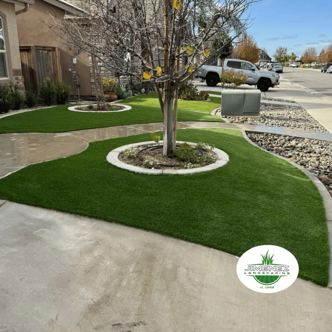 Lush artificial turf landscaping with decorative rock borders and a tree, designed by Jimenez Landscaping in Bakersfield, showcasing a vibrant outdoor space.
