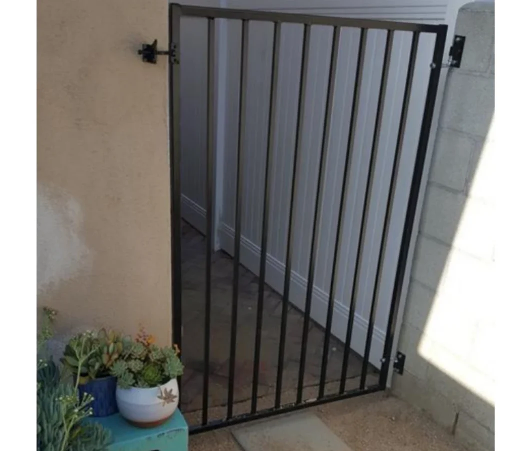 Black metal gate with vertical bars, leading to a landscaped area with potted succulents, showcasing Jimenez Landscaping's attention to detail in outdoor spaces in Bakersfield.