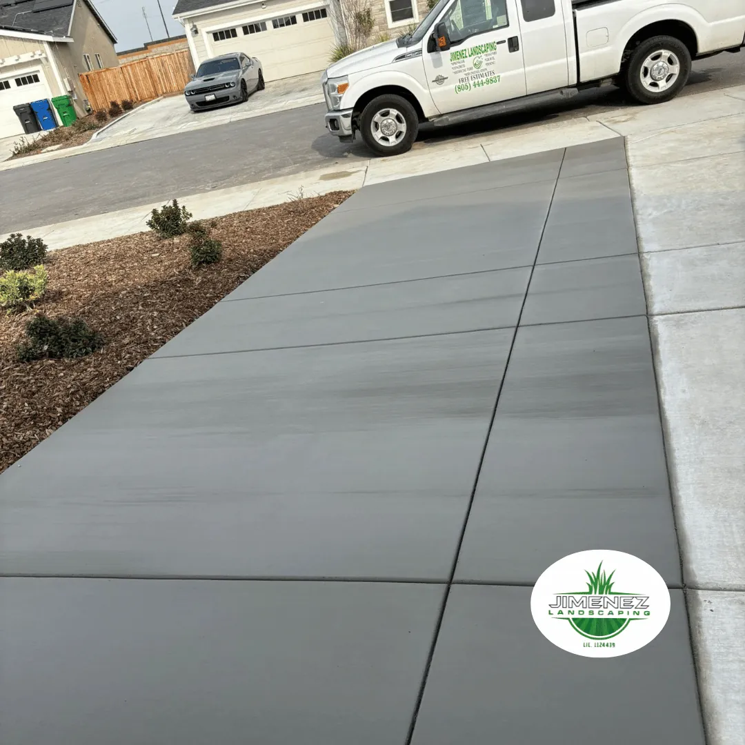 Newly installed concrete driveway by Jimenez Landscaping in Bakersfield, featuring smooth, gray slabs and surrounding landscaped areas.