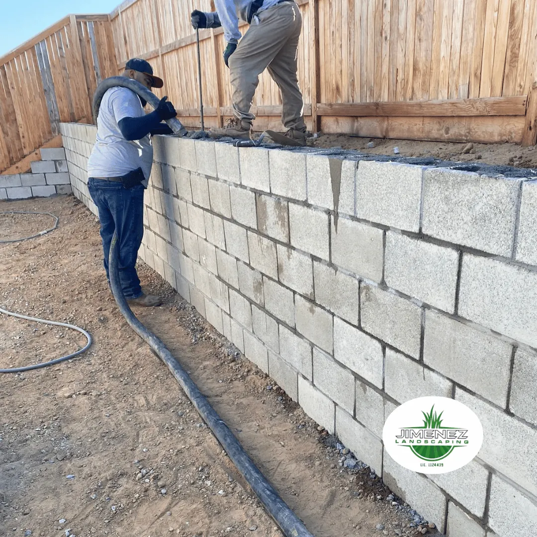 Two workers installing a concrete block wall for a fence in Bakersfield, showcasing Jimenez Landscaping's masonry services.