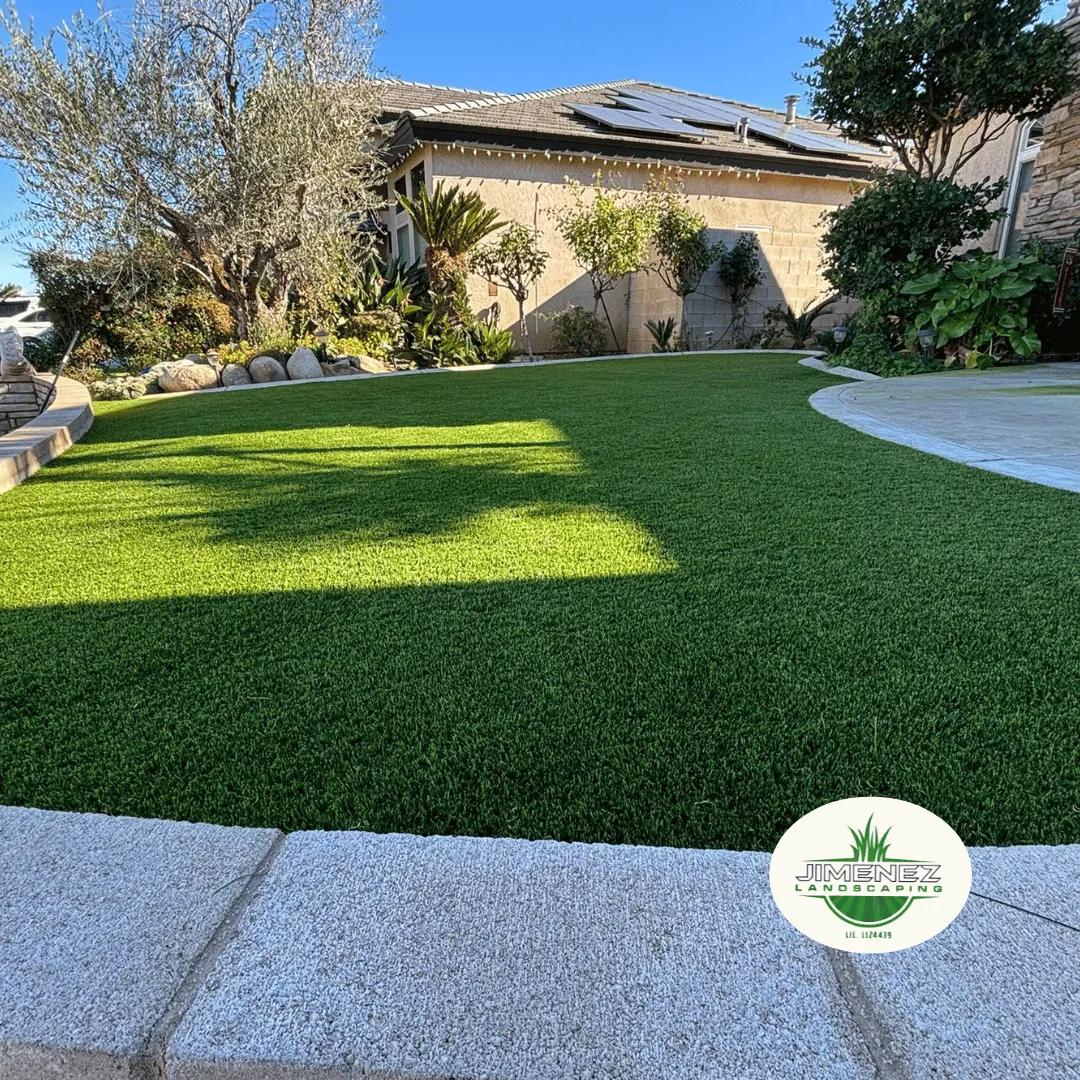 Lush artificial turf lawn in a residential Bakersfield yard, surrounded by ornamental plants and a stone pathway, showcasing Jimenez Landscaping's expertise in landscape design.